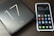A smartphone with a colorful app-filled screen is placed next to a sleek, black product box labeled '17 Pro'. The surface has a smooth and glossy finish, reflecting light subtly.
