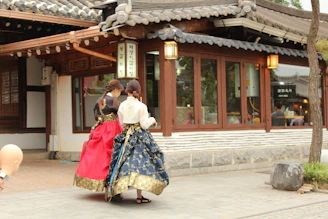 A vibrant street in Seoul with locals and tourists wearing colorful hanboks amid historic buildings.