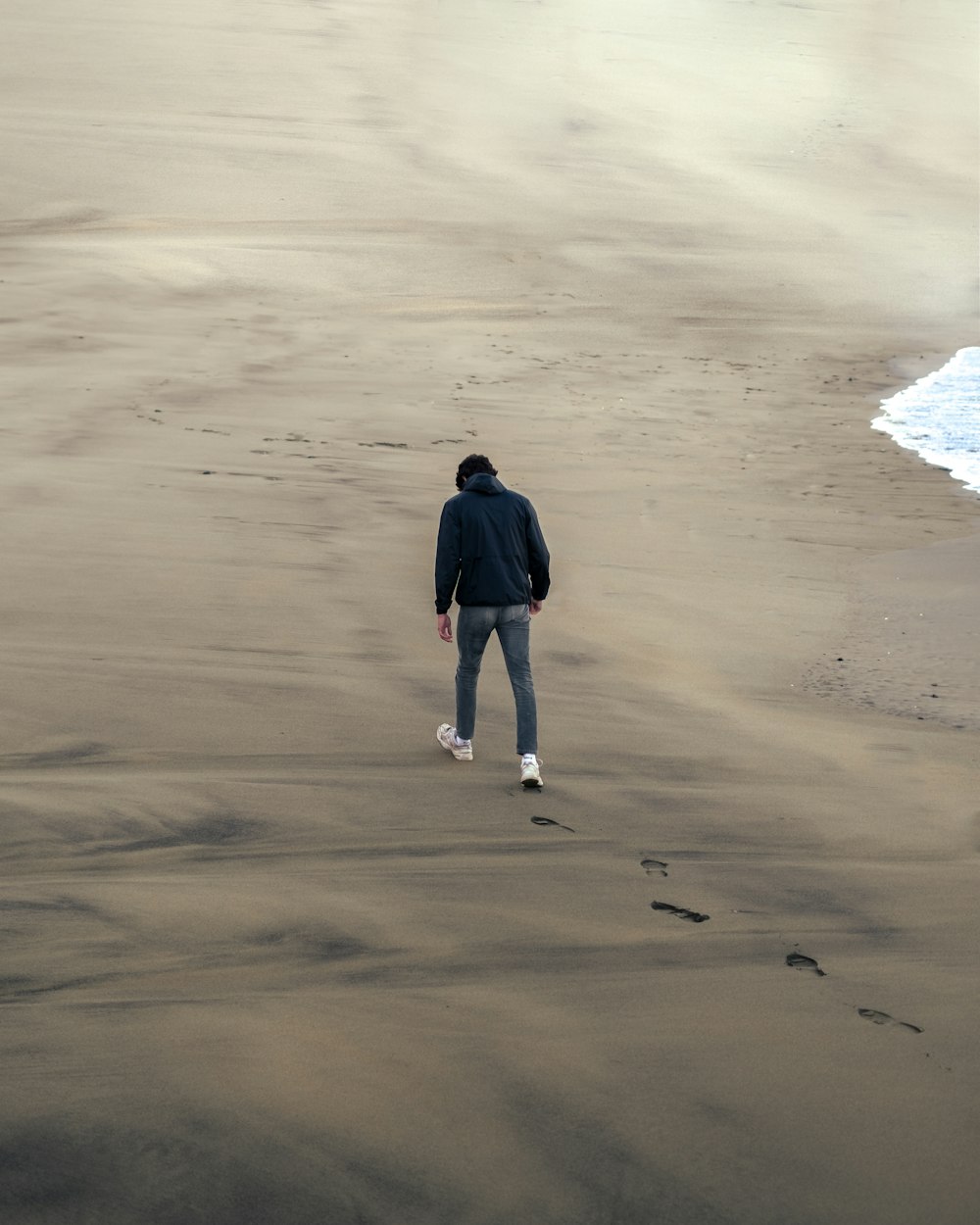 woman in black long sleeve shirt and blue denim shorts walking on seashore during daytime