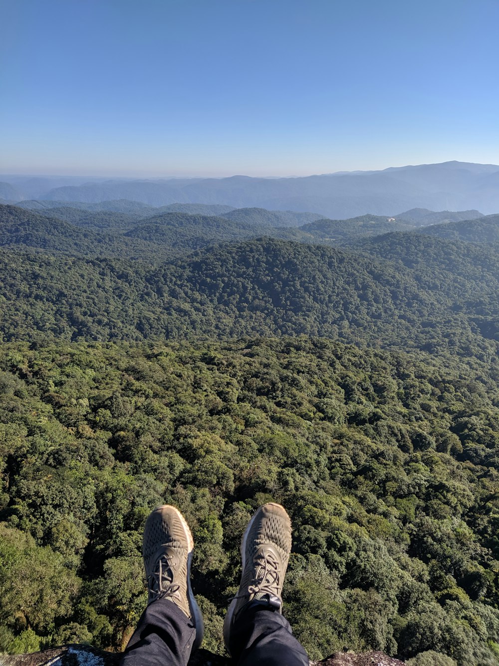 person in black and white sneakers sitting on top of mountain during daytime