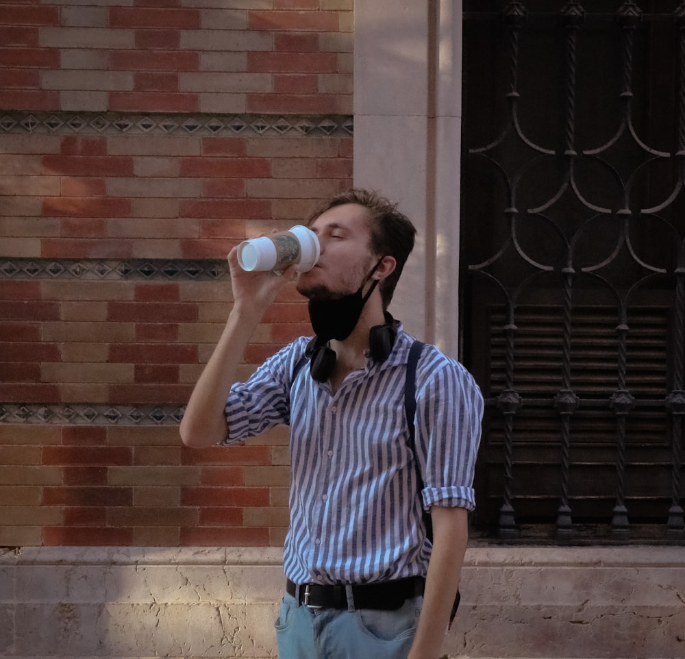man in blue and white stripe button up shirt drinking from white cup