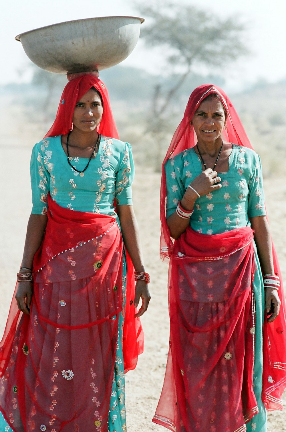 2 women in blue and pink dress standing on brown sand during daytime