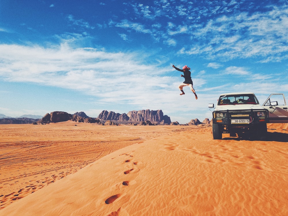 man jumping on brown sand under blue sky during daytime