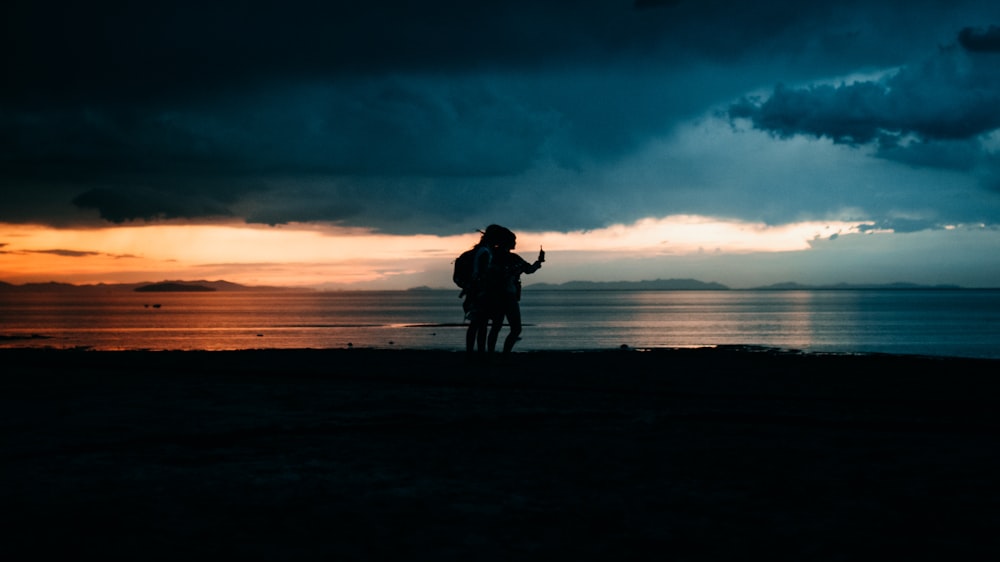 Silhouette von Mann und Frau, die während des Sonnenuntergangs am Strand spazieren gehen