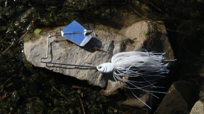 Brightly colored spinnerbaits glinting in natural sunlight beside a fishing rod.
