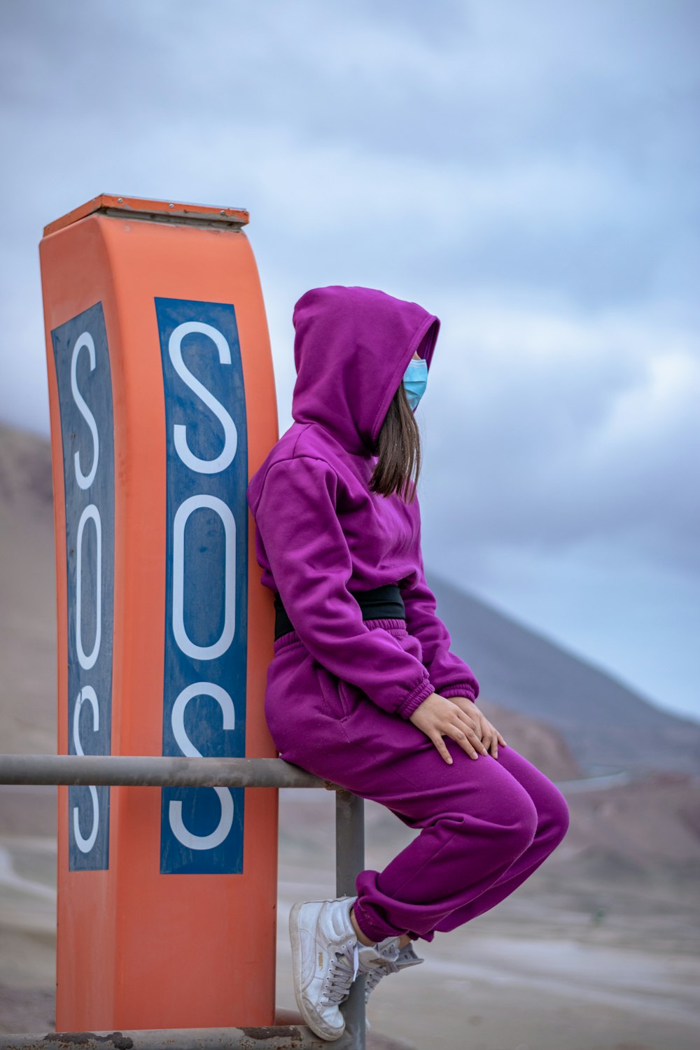 woman in purple hoodie and purple scarf standing on brown wooden fence during daytime