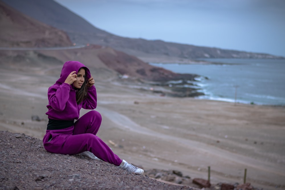 woman in purple hijab and purple long sleeve dress sitting on brown sand near body of near near near near
