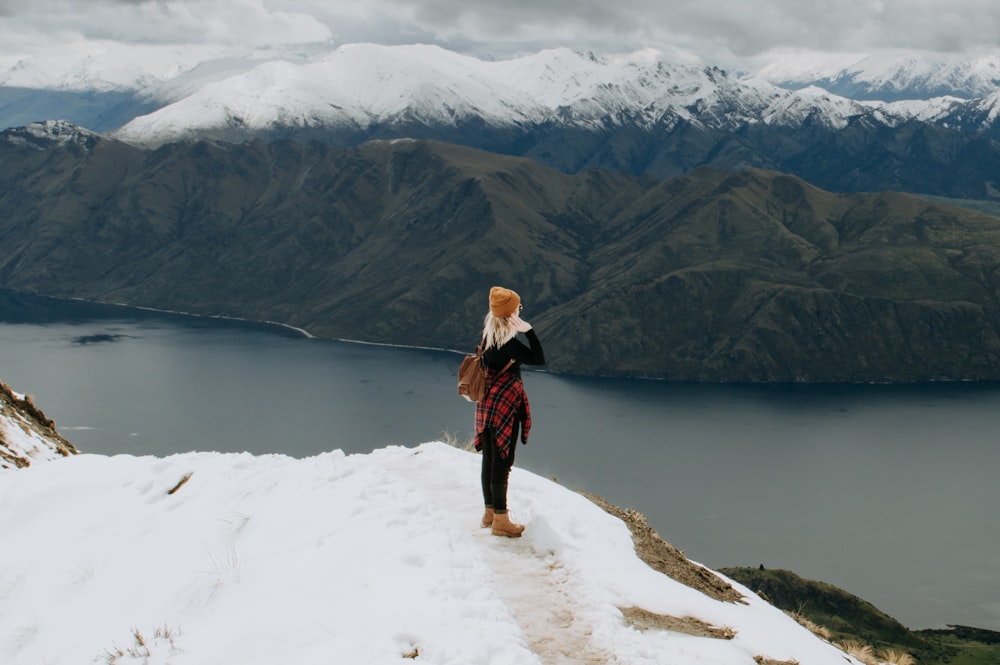 woman in black jacket and brown pants standing on snow covered ground near lake during daytime