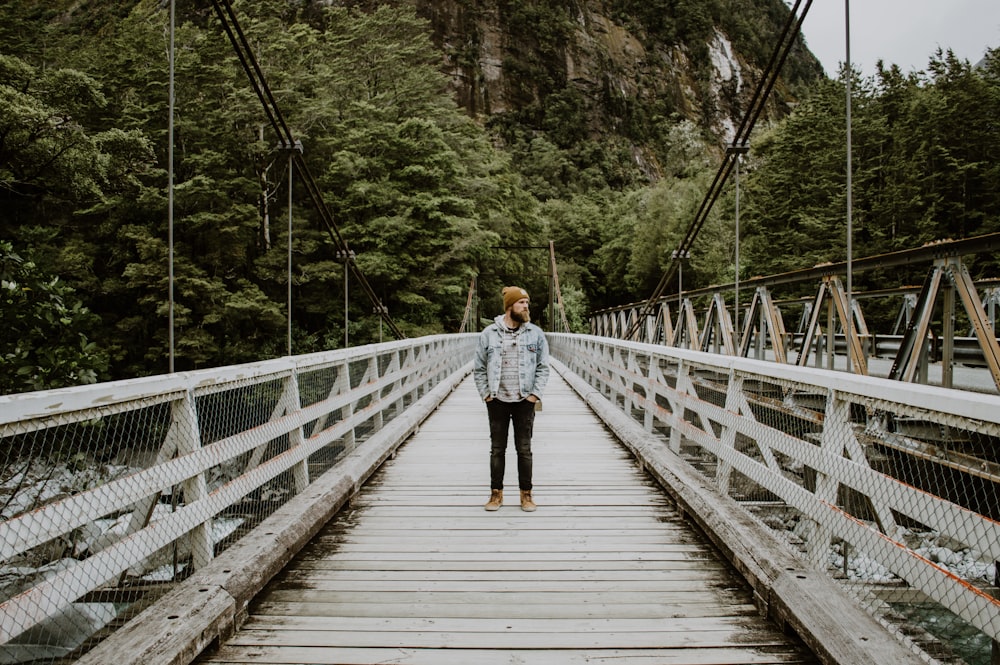 woman in black jacket and blue denim jeans walking on wooden bridge