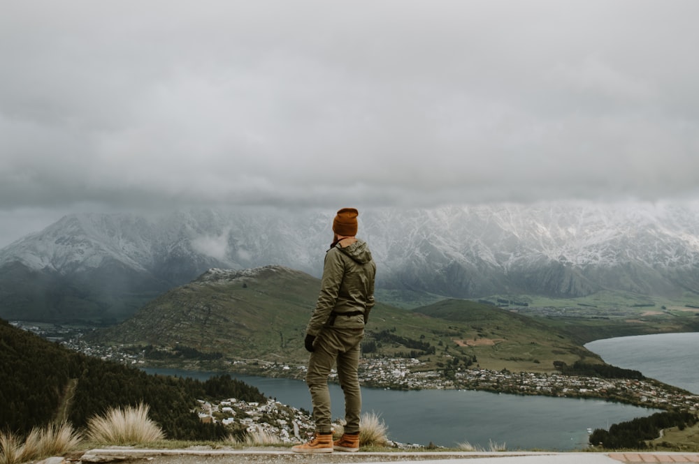 man in green jacket standing on rock near body of water during daytime