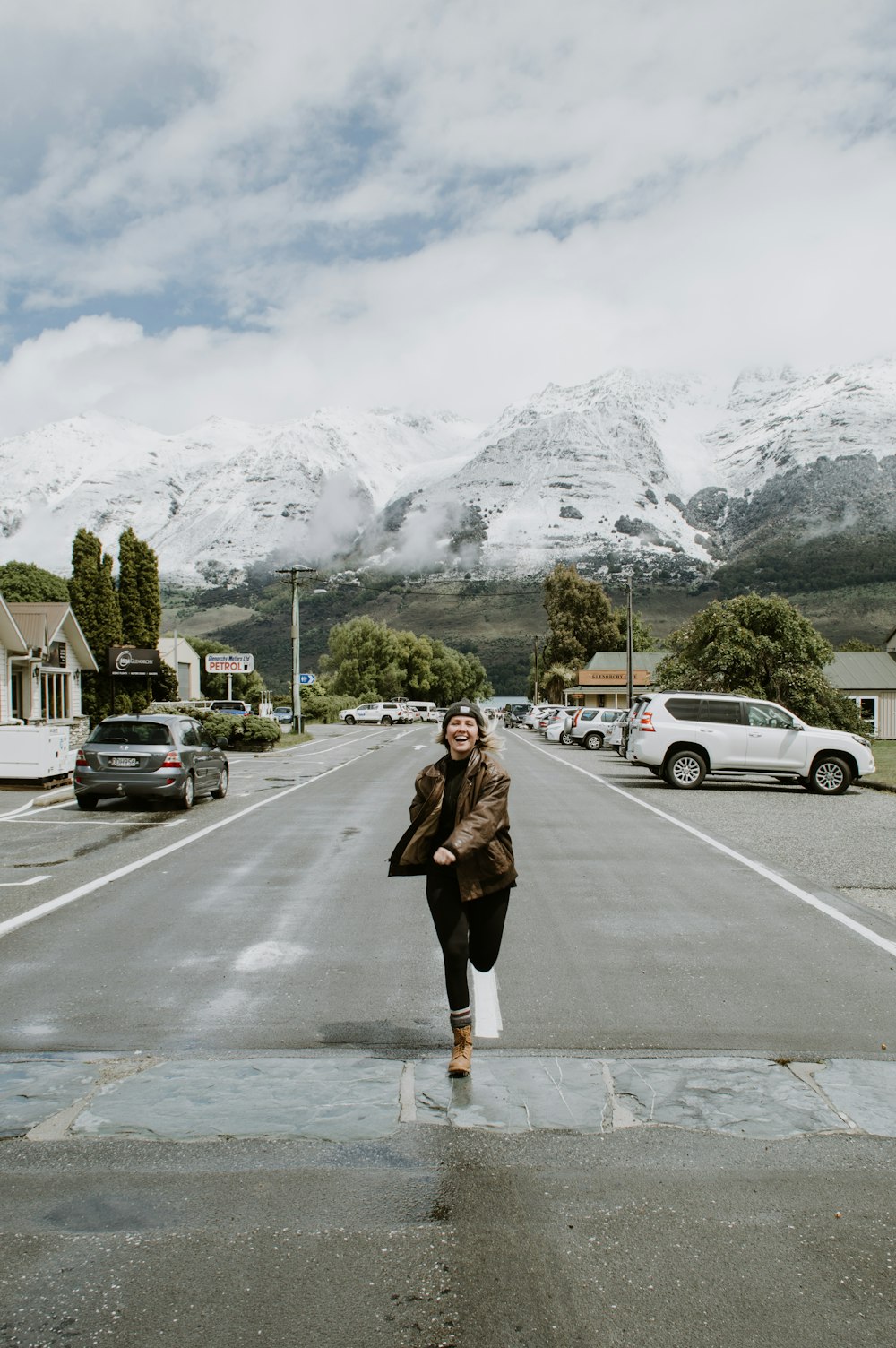 mulher em casaco marrom de pé na estrada perto da cordilheira durante o dia