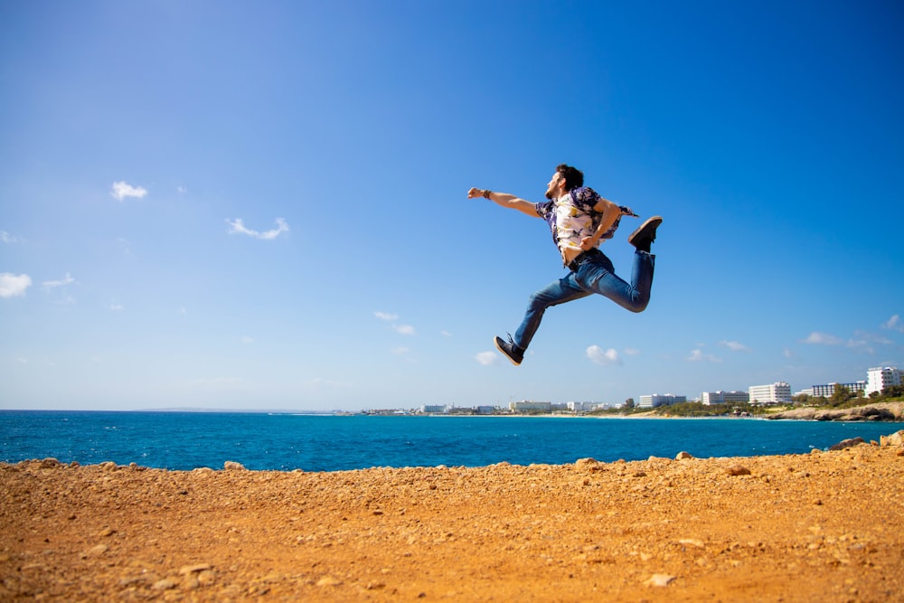 검은 셔츠를 입은 남자가 낮 동안 수역 근처의 갈색 모래 위에서 점프