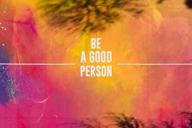 A vibrant abstract background featuring a blend of pink, orange, yellow, and purple hues. The words 'Be A Good Person' are centered in bold white text, with a thin white line extending horizontally from either side of the text.