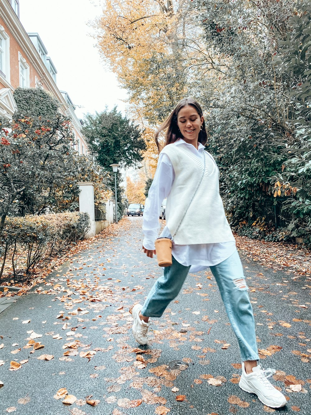 donna in cappotto bianco in piedi su foglie marroni durante il giorno