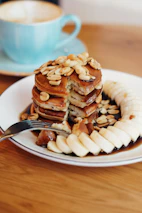 Cozy kitchen scene with freshly baked mini hotcakes stacked and garnished with banana slices and nuts.