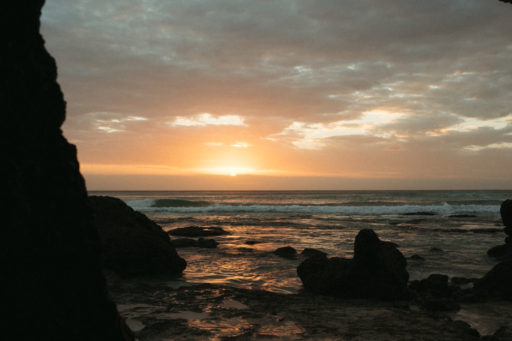 silhouette of rocks on sea shore during sunset