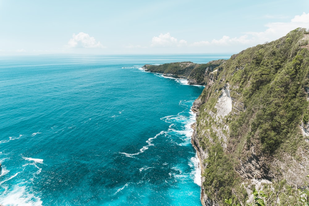 green and brown mountain beside blue sea under blue sky during daytime