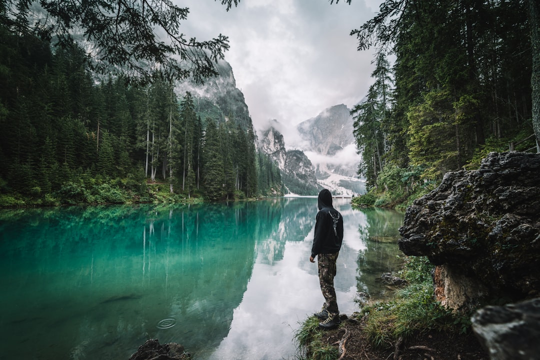 man in black jacket and pants standing on rock near river during daytime