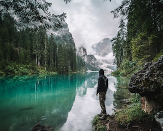 man in black jacket and pants standing on rock near river during daytime