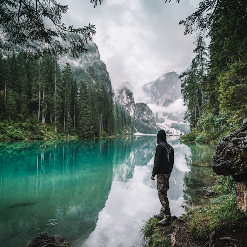 man in black jacket and pants standing on rock near river during daytime