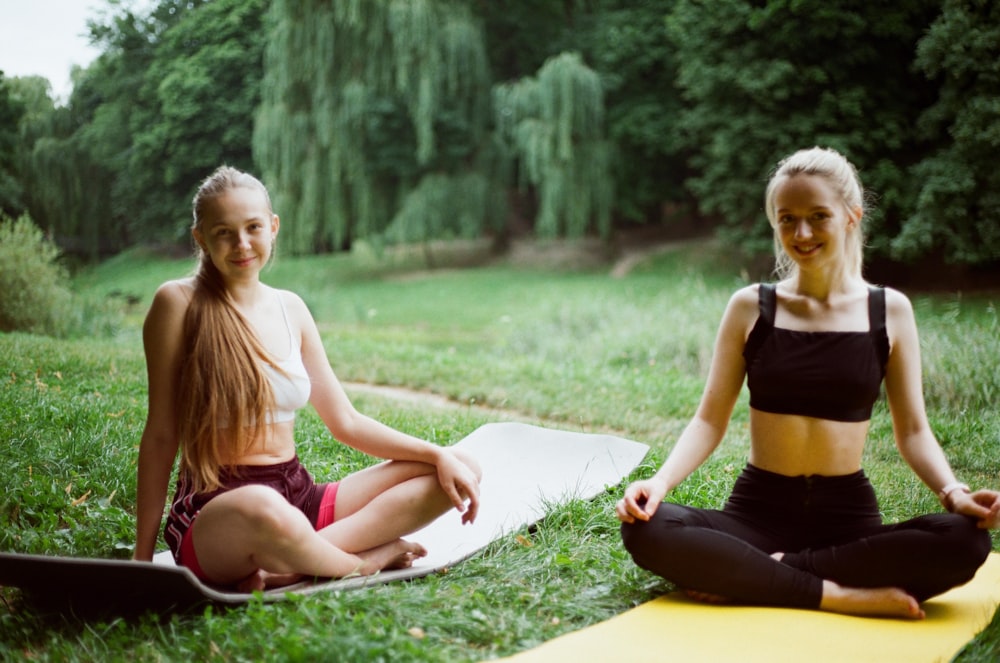 2 women in black tank top and black leggings sitting on green grass during daytime