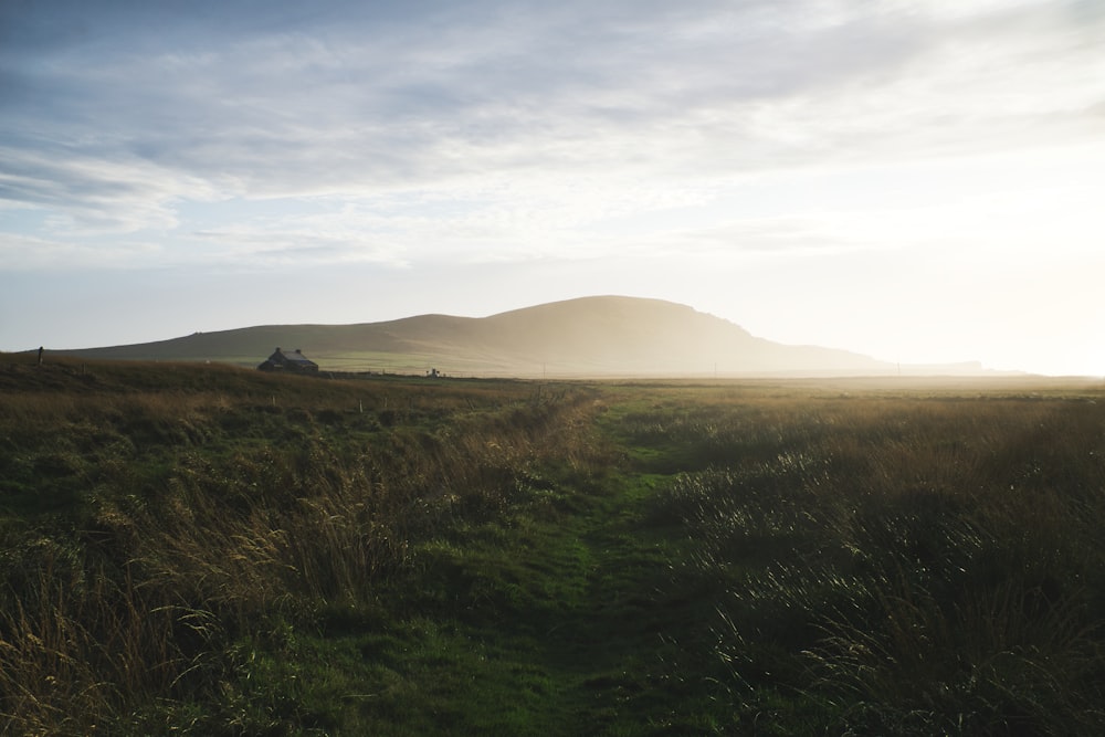 green grass field near mountain under white clouds during daytime