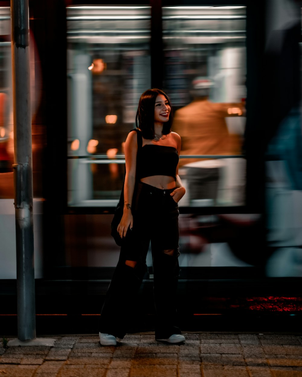 woman in white tank top and black pants standing on sidewalk during night time