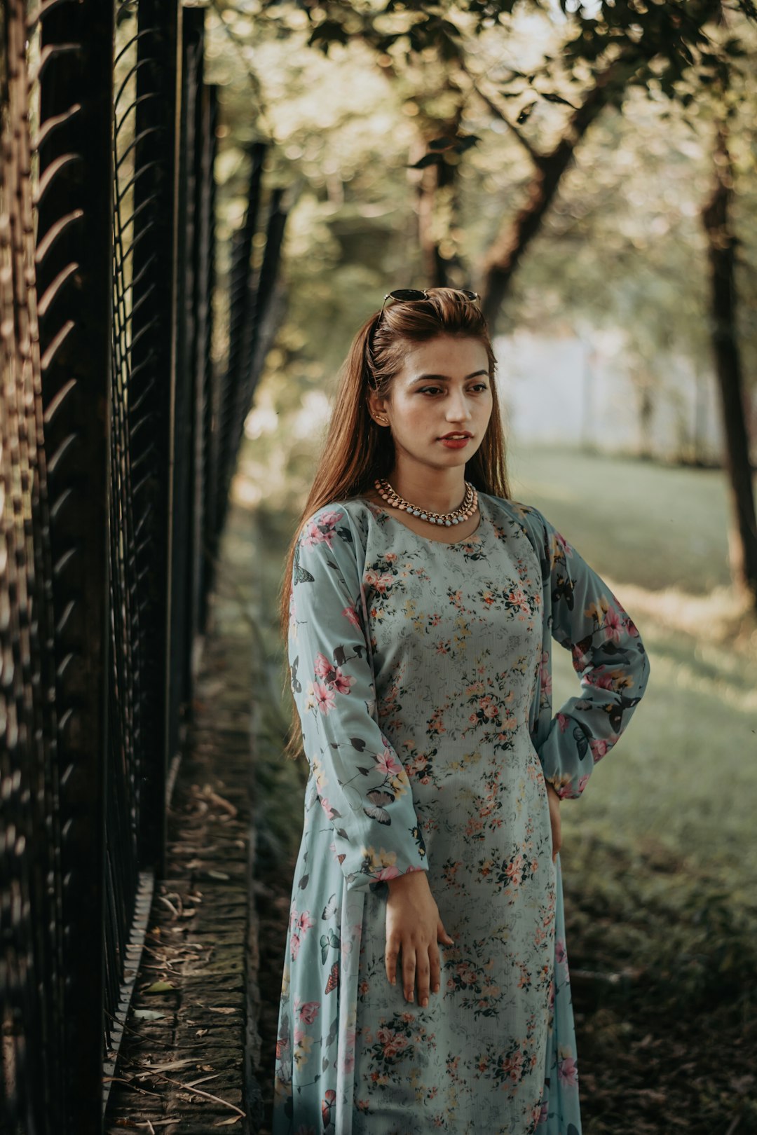 woman in blue and white floral dress standing near brown wooden fence