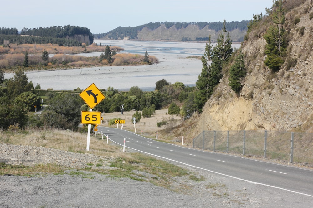 yellow and white road sign near body of water during daytime