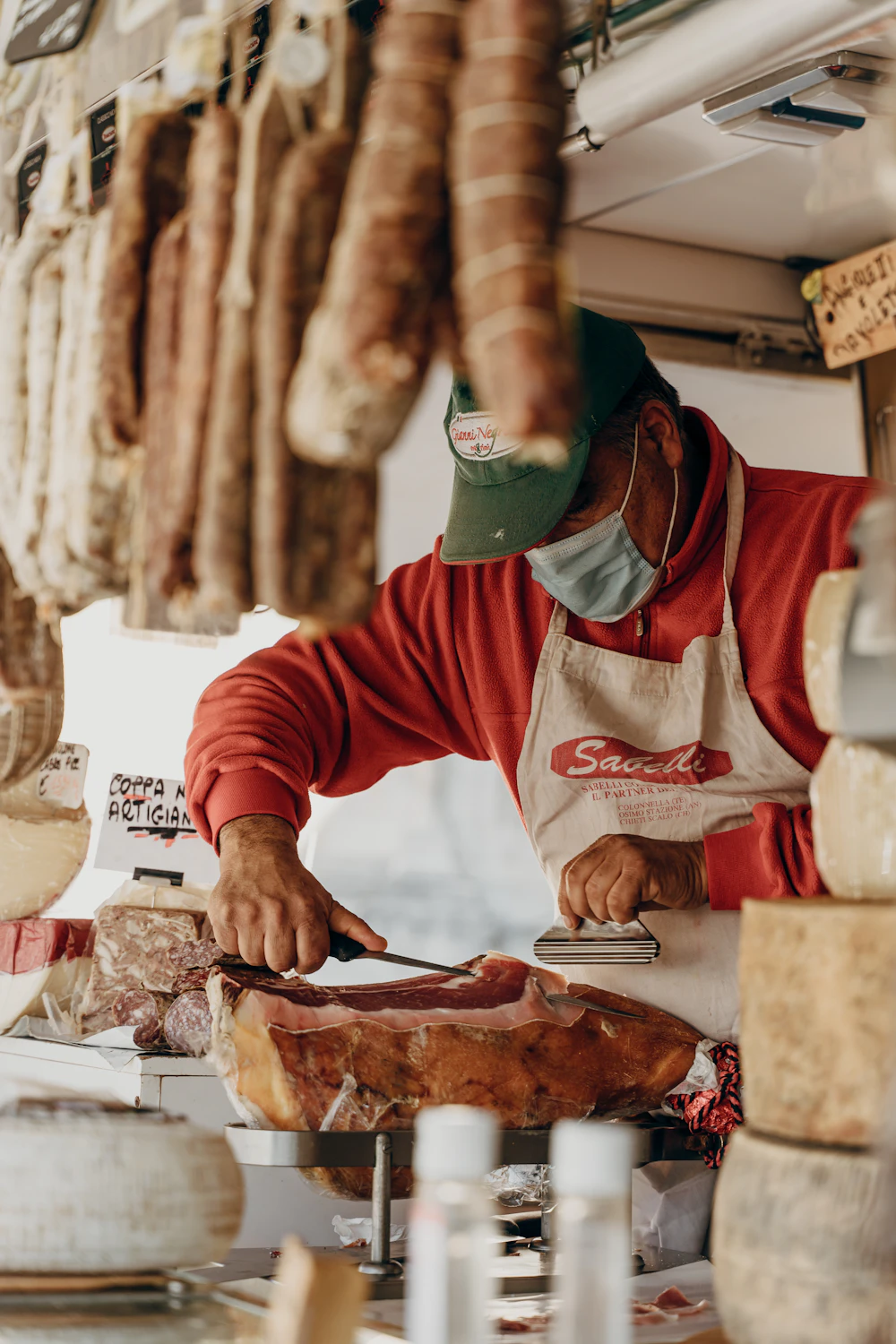 A deli worker slicing cured Italian meat behind the counter