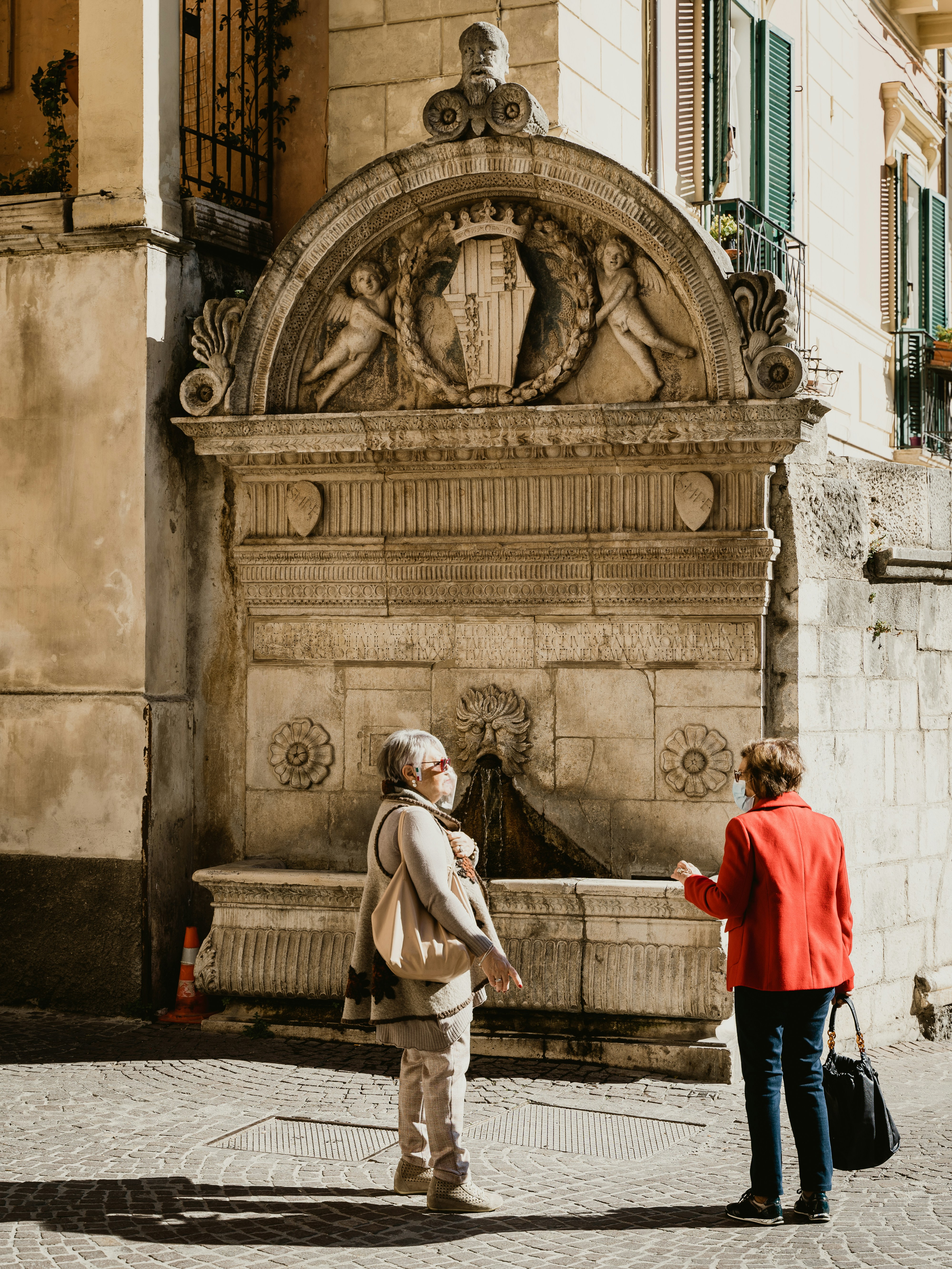 Two women chat in front of an antique fountain in the city of Sulmona, Abruzzo, Italy