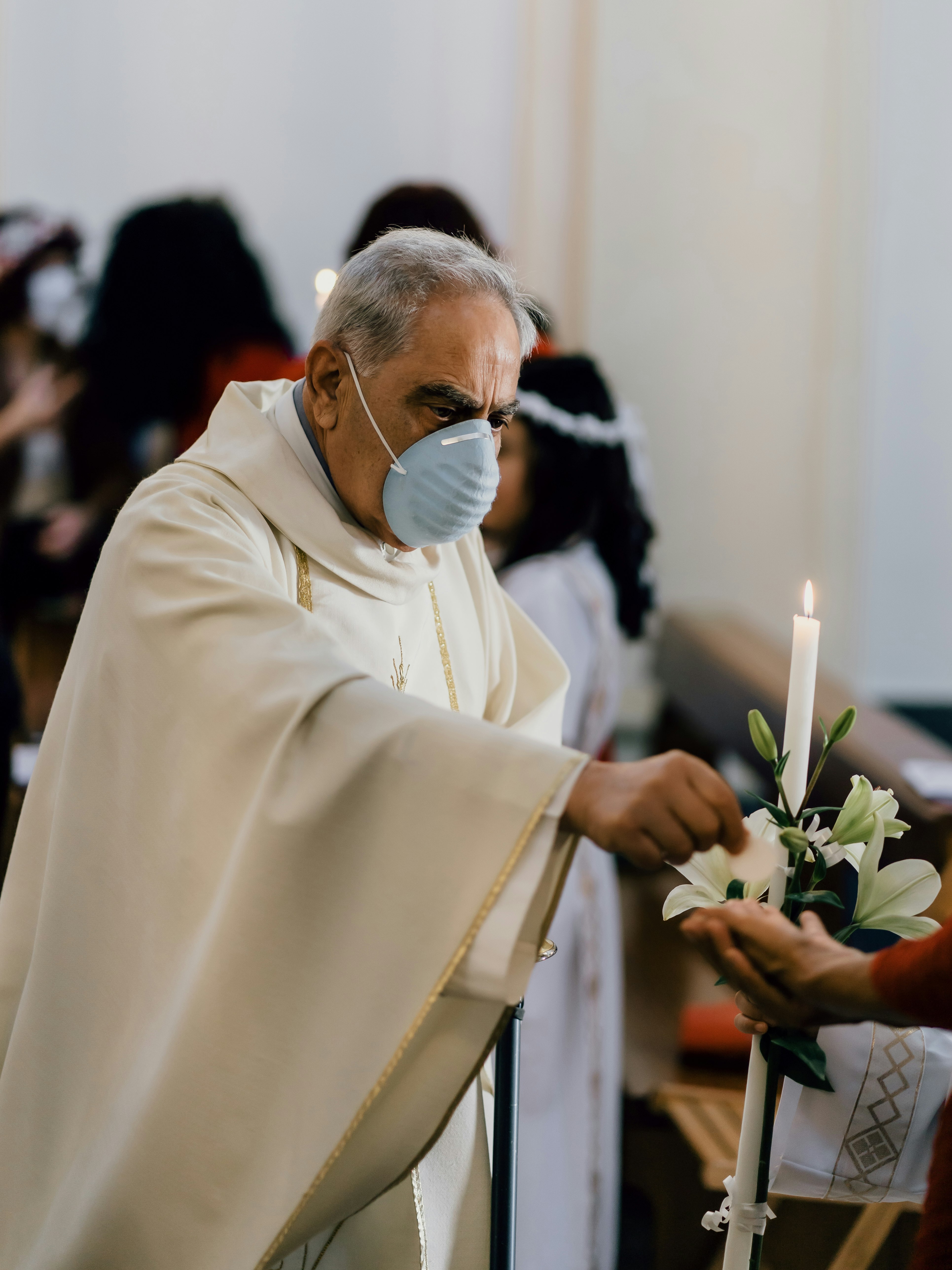 A Catholic priest wearing a face mask places a Sacred Host in outstretched hands during Holy Communion