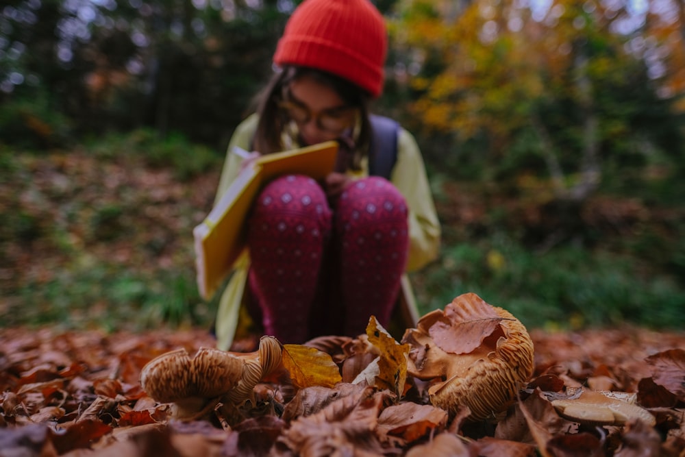 girl in green shirt and red pants sitting on dried leaves during daytime