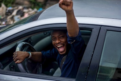 man in black t-shirt and blue denim jeans sitting on car seat