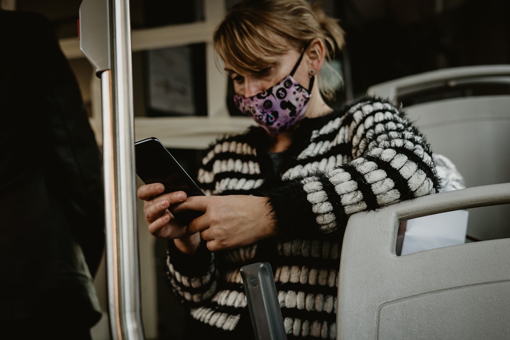 woman in black and white striped sweater wearing white mask holding black smartphone