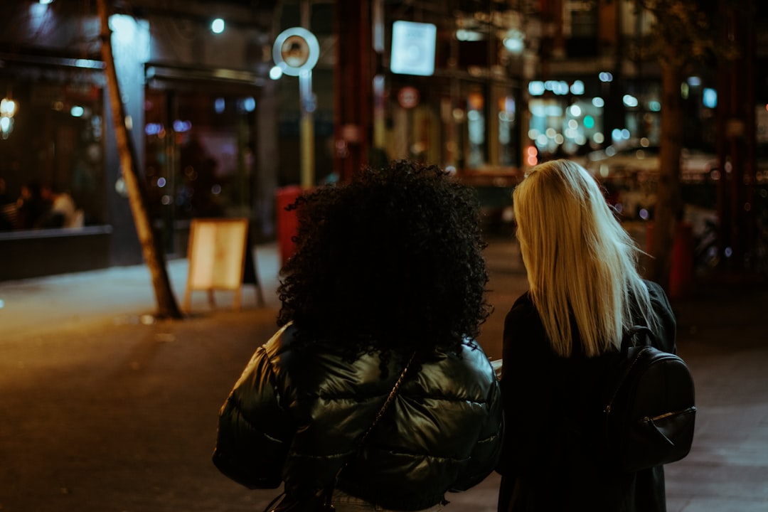 woman in black leather jacket standing on sidewalk during night time