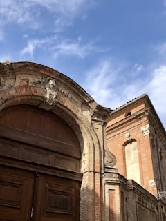 Historic two-story grey lodge building with classic Masonic square and compass emblem displayed prominently on the facade under a clear blue sky.