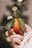 A hand delicately holds a small tangerine with two large green leaves attached. The background is softly blurred, creating a bokeh effect with circular light spots.