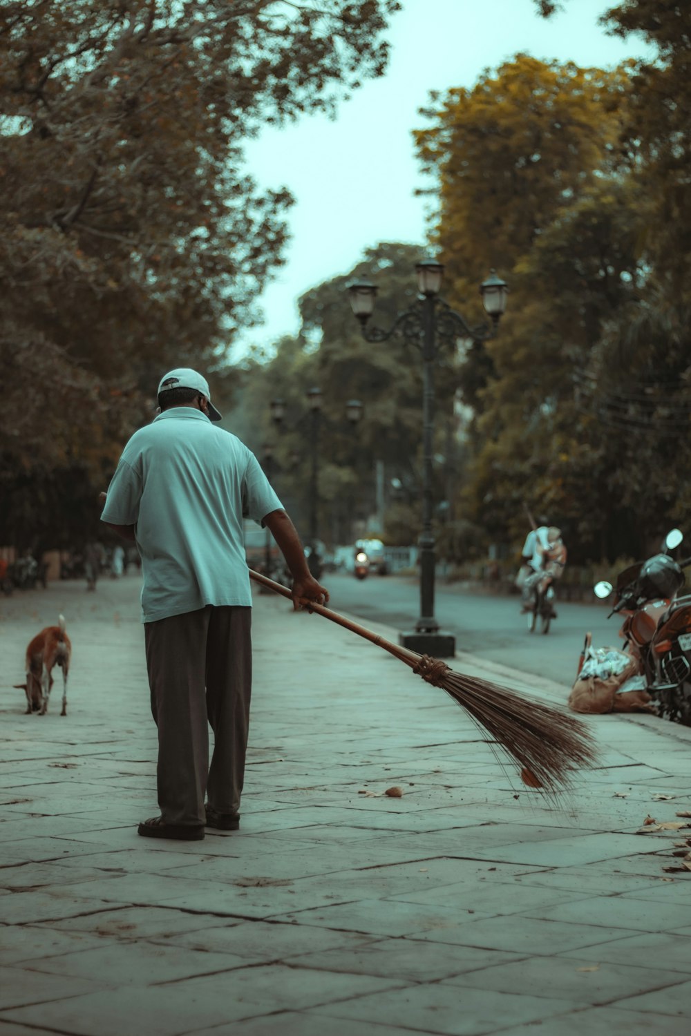 man in white t-shirt and black pants holding broom walking on street during daytime