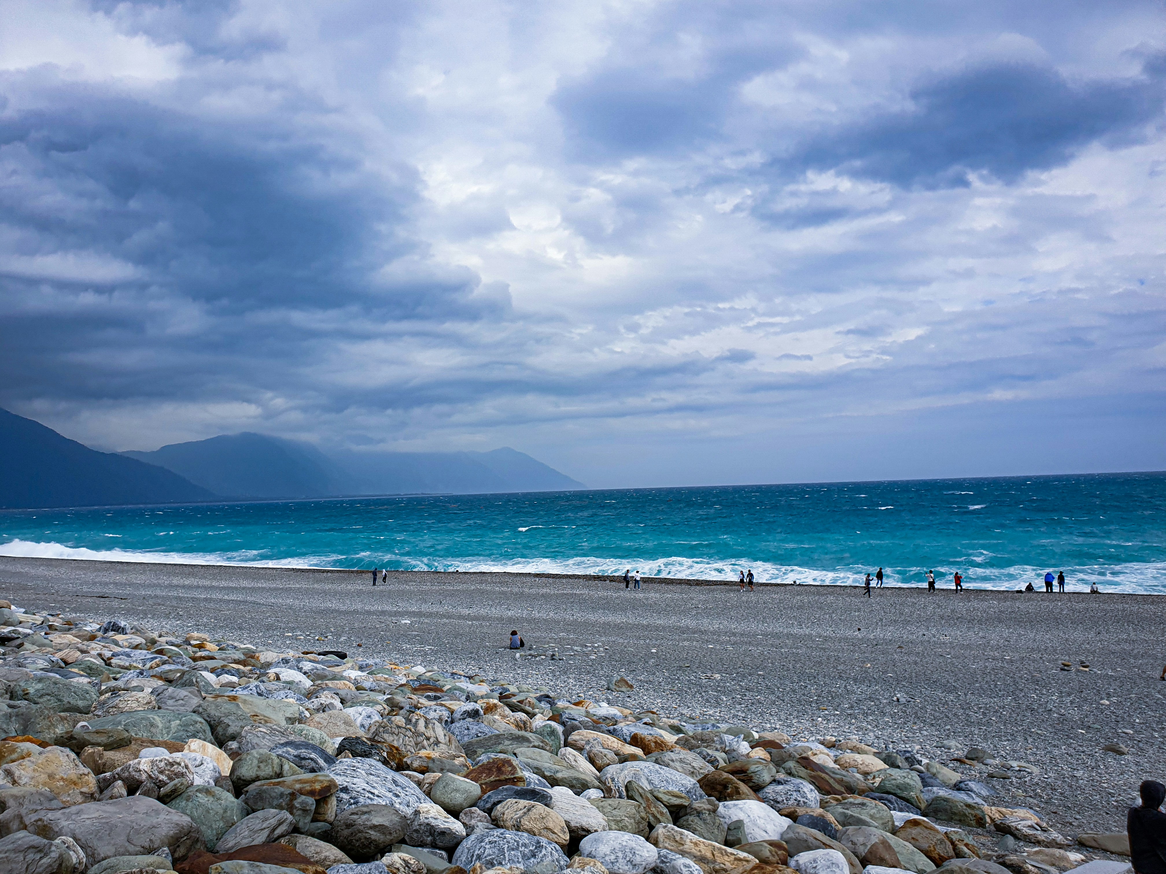 昼間の曇り空の下、海岸に浮かぶ灰色の岩
