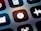 A close-up view of a mobile device screen displaying application icons in a grid layout. Visible icons include a stopwatch, a sound wave, an alarm clock, and other utility symbols. The design is sleek with icons having a minimalist, monochromatic style against a dark background.