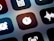 A close-up view of a mobile device screen displaying application icons in a grid layout. Visible icons include a stopwatch, a sound wave, an alarm clock, and other utility symbols. The design is sleek with icons having a minimalist, monochromatic style against a dark background.