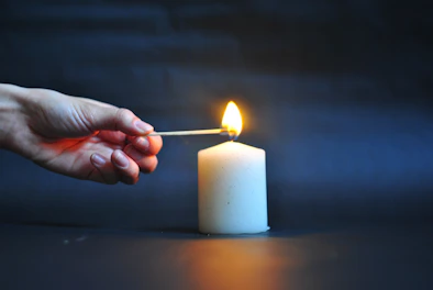 Close-up of a hand lighting a candle wick with a matchstick.