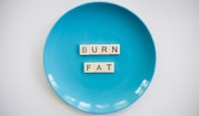 A blue plate with the words 'BURN FAT' spelled out in letter tiles placed in the center. The background is white which contrasts with the blue plate.