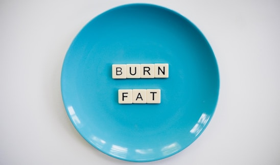 A blue plate with the words 'BURN FAT' spelled out in letter tiles placed in the center. The background is white which contrasts with the blue plate.
