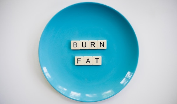 A blue plate with the words 'BURN FAT' spelled out in letter tiles placed in the center. The background is white which contrasts with the blue plate.