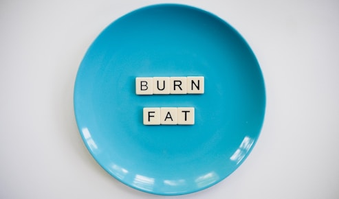 A blue plate with the words 'BURN FAT' spelled out in letter tiles placed in the center. The background is white which contrasts with the blue plate.