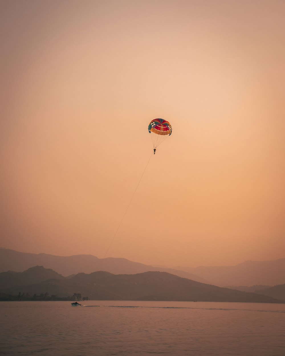 paracadute rosso e bianco sopra le montagne durante il tramonto