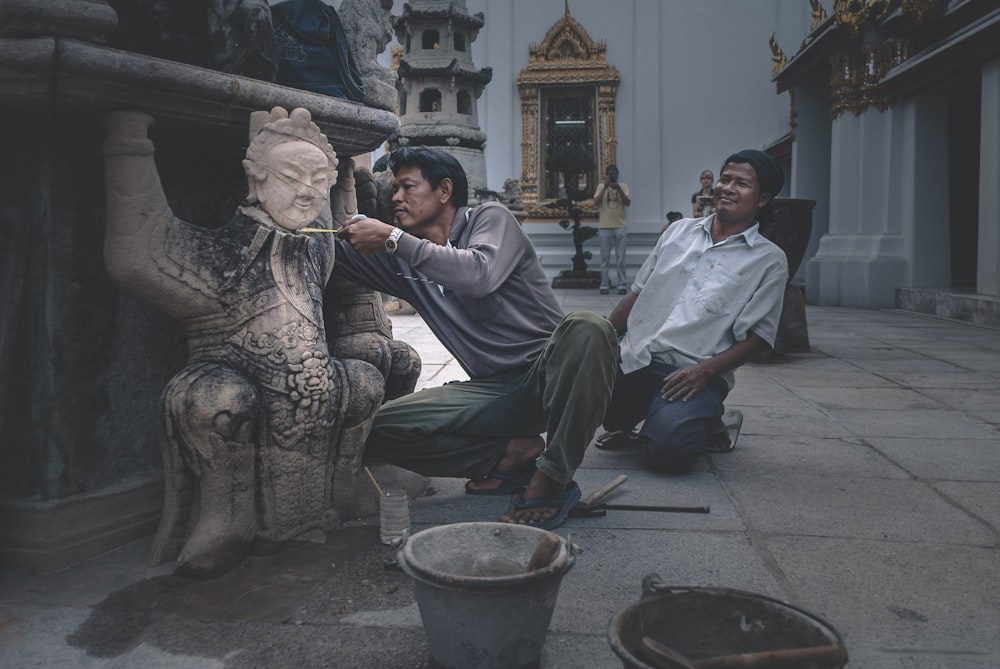 man in gray long sleeve shirt sitting on gray concrete statue during daytime