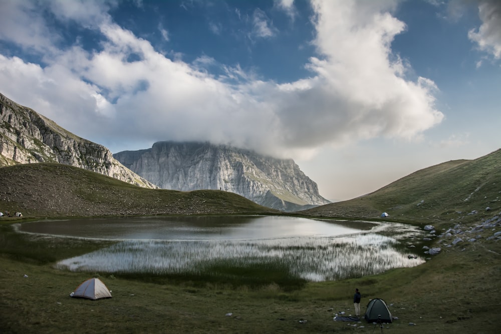 white tent on green grass field near mountain under white clouds and blue sky during daytime